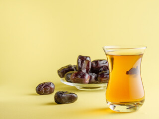 Tea in a traditional Turkish mug with dates in the background, on a yellow background. Traditional iftar food.