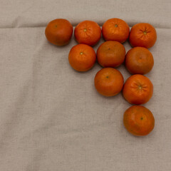 Bright tangerines are laid out in a triangle shape. Background - beige napkin. Top right corner. Copy space