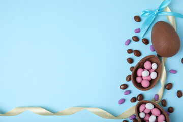 Flat lay composition with tasty chocolate eggs and candies on light blue background. Space for text