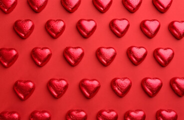 Fototapeta na wymiar Heart shaped chocolate candies on red background, flat lay