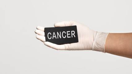Closeup of the hand in a white sterile glove holding a card with word - CANCER