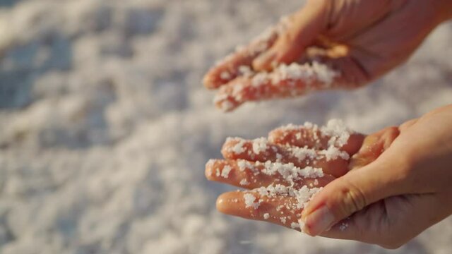 Top view slow motion closeup woman hands holding crystallized salt natural mineral formation at Dead Sea coastline with highlight sunlight