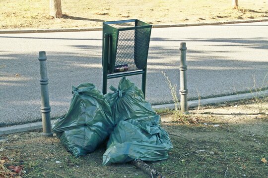 Dos bolsas de basura junto a una papelera de un parque público. Basura esperando a ser recogida en una calle de la ciudad de Madrid.