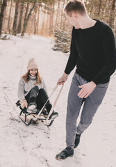 
A man rolls a woman on a sled in the forest