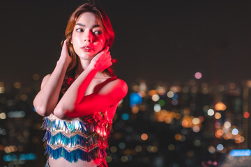 Naklejka premium Young asian woman dancing and celebrating party new year.Young trendy ambitious woman looking intense in the camera at night next to neon light. Nightlife youth and urban atmosphere.