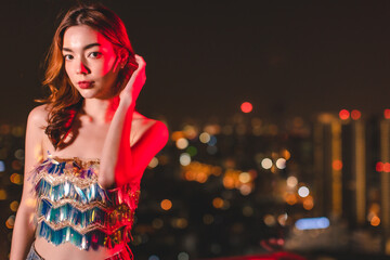 Beautiful young asian brunette woman with white dress joying Christmas or New Year night on a city.Woman holding sparkler against defocused lights, close up.