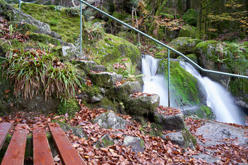 Part of a brown seat bench in the forest, stone stairs lead upwards. Beautiful waterfall in the...