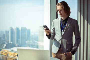 Businessman using mobile phone app texting outside of office in urban city with skyscrapers buildings in the background. Young Handsome Business CEO caucasian man holding smartphone for business work.