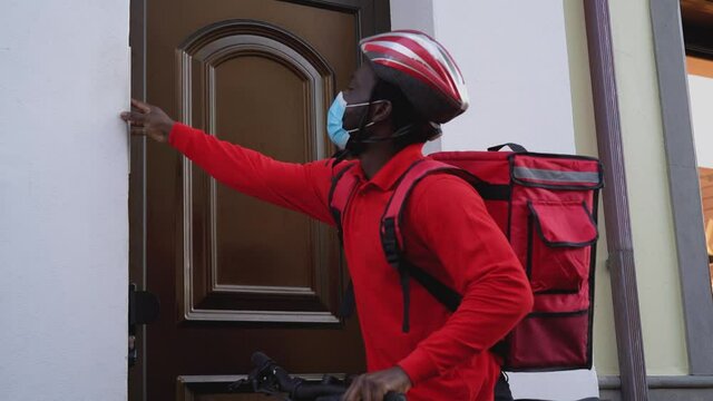 African rider man delivering meal to customers home with electric bicycle while wearing face mask during corona virus outbreak - Ecological fast delivery food concept