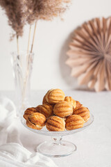 Russian traditional homemade cookies Nuts with condensed milk on glass stand on background of paper decor and reeds in vase White background, selective focus