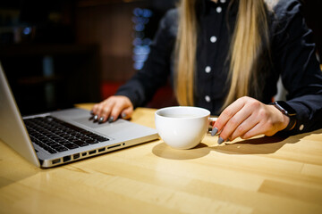 Young woman holding a cup of coffee and using laptop computer. Businesswoman working from home. Online shopping, e-commerce, work from home