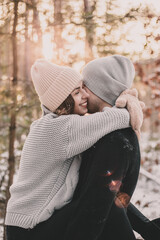 
Woman hugs a man dressed in mittens in a pine forest