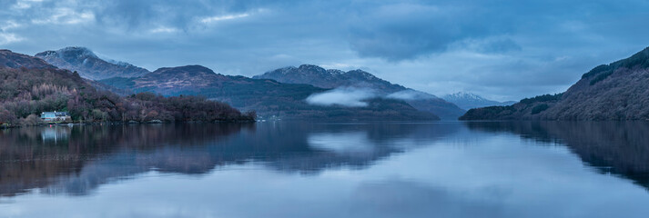 Majestic landscape image across Loch Lomond looking towards snow capped Ben Lui mountain peak in Scottish Highlands