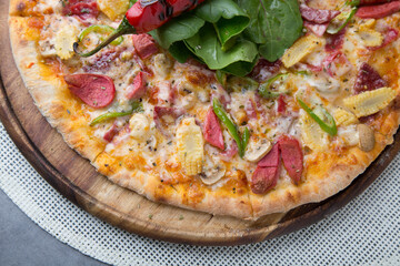 Pizza with sausage, cheese, baby corn, rocket leaves and roasted red pepper on wooden pizza plate 