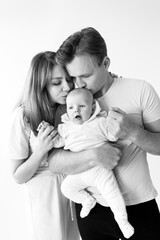 Black and white photo of a young caring family with a small child in their arms. The parent gently kisses the baby, photographed as a keepsake, enjoying the moment. Family concept.