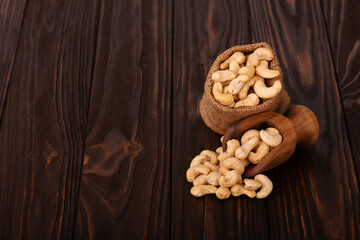 Cashew nuts in bag and wooden scoop, on wooden background. Roasted cashew nuts.