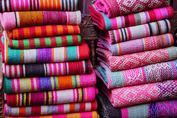 Two heaps of multi coloured traditional Peruvian woven textiles at a street market, Peru