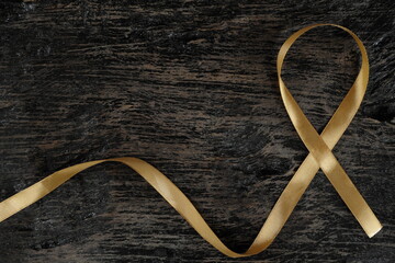 Top view of gold ribbon on dark wood background. Childhood cancer awareness concept.	