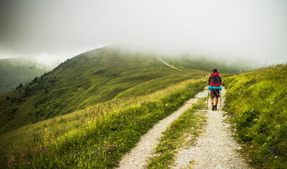 Obraz premium Hiker walking on a meadow walking into a cloud on rainy day