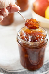 Homemade apple jam marmalade with cloves and cinnamon from organic apples in a transparent glass jar with vintage retro spoon in woman female hand. Homemade autumn jam preserves.