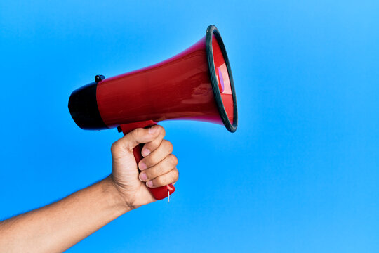 Hand of hispanic man holding megaphone over isolated blue background.