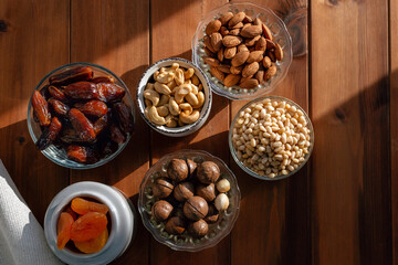 Different dried fruits and nuts under natural sunlight on wooden table. Overhead, from above