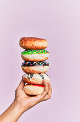 Hand of hispanic man holding tower of donuts over isolated pink background.