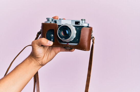 Hand of young hispanic man holding vintage camera over isolated pink background.