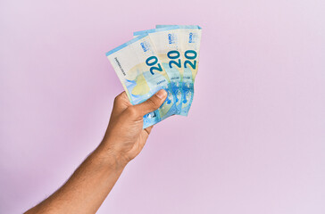 Hispanic hand holding 50 euro banknotes over isolated pink background.