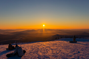 snowboarders meet the sunset from the top of a snowy mountain