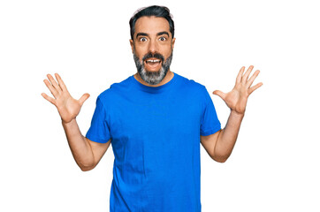 Fototapeta premium Middle aged man with beard wearing casual blue t shirt celebrating crazy and amazed for success with arms raised and open eyes screaming excited. winner concept