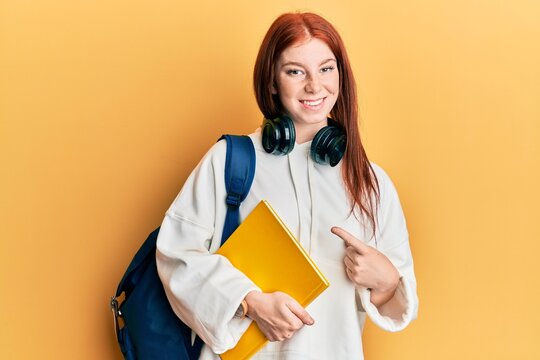 Young red head girl wearing student backpack and holding book smiling happy pointing with hand and finger