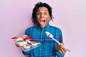 Young african american man eating sushi using chopsticks celebrating crazy and amazed for success...