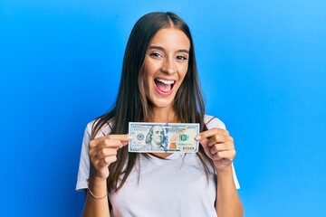 Young hispanic woman holding 100 dollar banknote smiling and laughing hard out loud because funny crazy joke.