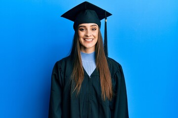 Beautiful brunette young woman wearing graduation cap and ceremony robe with a happy and cool smile on face. lucky person.