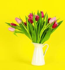 Beautiful spring flowers tulips in vase on yellow background. Festive concept