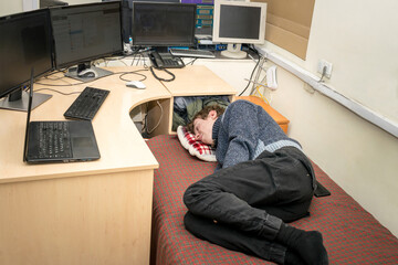 Tired guy sleeps in front of monitors in the office. The monitoring operator is lying on the bed. A man from the technical department sleeps on a bed at his workplace.