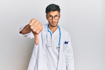 Young handsome man wearing doctor uniform and stethoscope looking unhappy and angry showing rejection and negative with thumbs down gesture. bad expression.