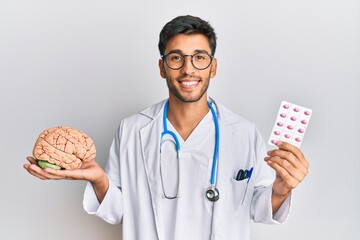 Young handsome man holding brain and pills as mental health concept smiling with a happy and cool...