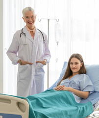 Obraz premium A senior older female doctor standing in an elegant pose put hands in pocket, and smile with kindness taking photos with a younger patient.