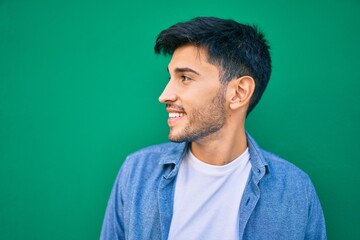 Fototapeta premium Young latin man smiling happy leaning on the wall at the city.