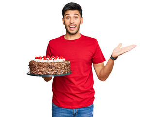 Young handsome man celebrating birthday with cake celebrating victory with happy smile and winner expression with raised hands