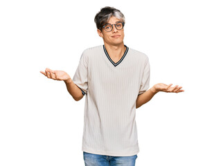 Young hispanic man wearing casual clothes and glasses clueless and confused expression with arms...