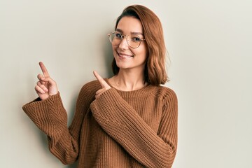 Young caucasian woman wearing casual clothes and glasses smiling and looking at the camera pointing with two hands and fingers to the side.