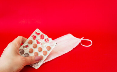 Pills in a woman's hand on a red background, next to a medical mask. Medicine concept.