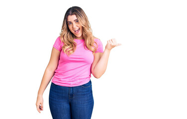 Young caucasian woman wearing sportswear smiling with happy face looking and pointing to the side with thumb up.