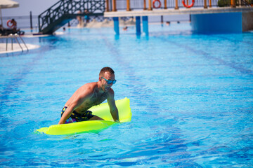 Handsome young man swims on inflatable mattress in blue pool