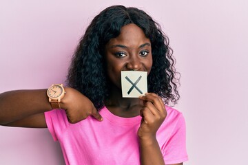 Beautiful african young woman holding paper with cross symbol pointing finger to one self smiling...