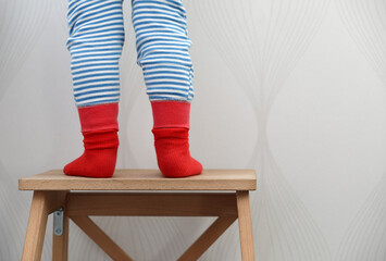 Children's legs in red socks and striped pants on a chair