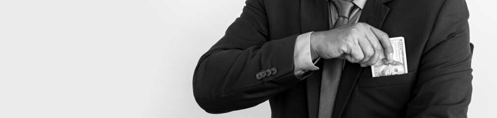 A black and white photo of a businessman taking a dollar out of his pocket, businessman concept. panorama banner background. © kamiphotos